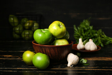 Bowl with green tomatoes and garlic on dark wooden table