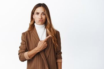 Portrait of unamused and disappointed businesswoman pointing finger at upper right corner, grimacing dissatisfied, showing advertisement, white background