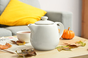 Tea pot and autumn leaves on table in room