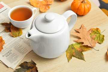 Tea pot, cup of hot beverage, newspaper and autumn leaves on wooden background