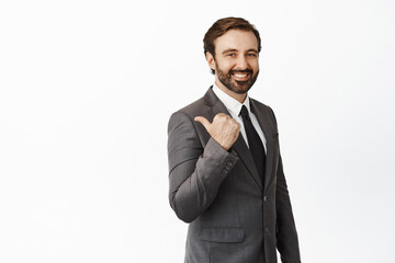 Handsome corporate man in business clothes pointing left, inviting clients, showing company sign and smiling, standing over white background
