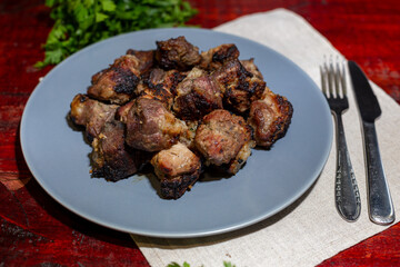 Shashalyk - pieces of pork fried over charcoal with shallots, sauce and herbs on a slate tray with a dark background.