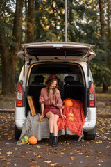 beautiful caucasian girl sitting in a car in the fall in a sweater hat and short skirt. Near easel