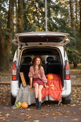 beautiful caucasian girl sitting in a car in the fall in a sweater hat and short skirt. Near easel