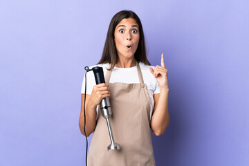 Brazilian woman using hand blender isolated on purple background intending to realizes the solution while lifting a finger up