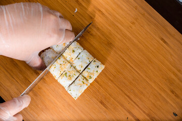 A sushi chef slicing a roll of tempura maki with a sharp stainless knife on a cutting board. Making sushi rolls. © Mdv Edwards