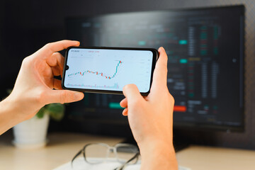 Business and finance, investment, trading and technology. Close-up businessman trader analyzing cryptocurrency stock market investing in bitcoin, workplace. Profit growth and loss graph on smartphone