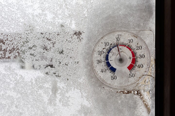 Thermometer on glass covered with snow and ice on a cloudy winter day. Natural disasters caused by...