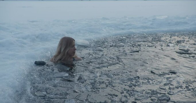 Winter ice hole swimming woman in ice cold water in frozen lake
