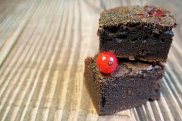 two pieces of gluten-free brownie with red currants lie on a wooden background. gluten-free and lactose-free cakes. homemade cakes