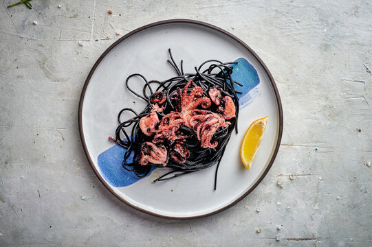 Baby octopus on a plate with nero di seppia. black pasta squid ink. On dark rustic background