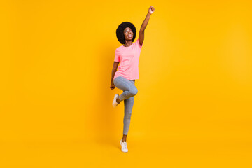 Full length photo of impressed young lady look empty space arm up wear pink t-shirt jeans isolated on yellow color background