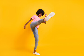Full length photo of funky young lady fight wear pink t-shirt jeans sneakers isolated on yellow color background