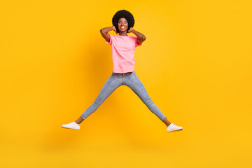 Fototapeta na wymiar Full length photo of cool millennial lady jump touch hair wear pink t-shirt jeans isolated on yellow color background