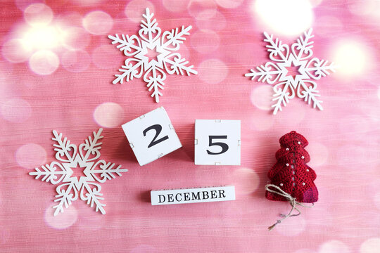 Calendar for December 25: cubes with the number 25, the name of the month in English, decorative snowflakes and a Christmas tree on a pink background, bokeh - Powered by Adobe