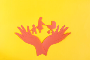 Cardboard figurines open palms of hands hold a woman with a stroller and a child. The concept of family and child protection