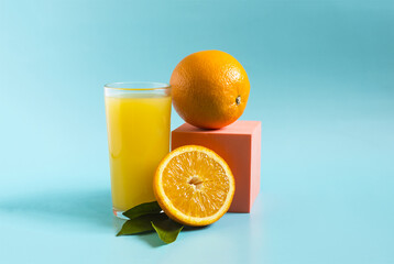Fresh orange juice in a transparent glass with a decor of oranges and green leaves on a blue background	