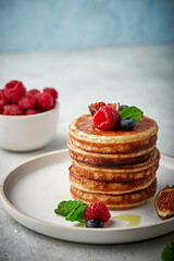 Tasty appetizing homemade pancakes served with honey, raspberries and blueberries on plate on grey background