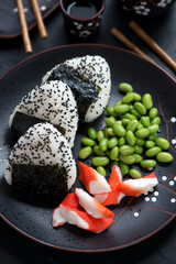 Close-up of japanese onigiri on a black plate with crab meat and edamame beans, vertical shot, selective focus