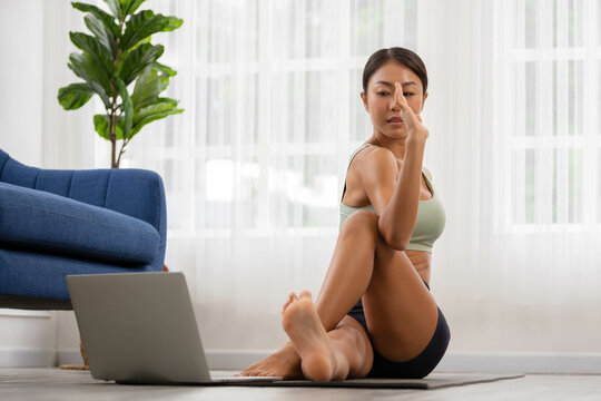 In the fitness studio, an Asian woman is studying online fitness training. Improve your health by extending meditating.