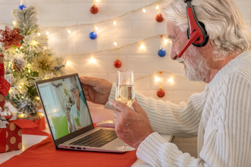 Smiling senior man in video call with laptop computer celebrating Christmas with a glass of sparkling wine. Happy new year and merry Christmas