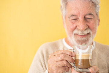 Defocused handsome bearded senior man holding a glass of coffee and milk, cappuccino, standing on yellow background