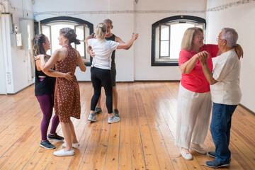 Senior Caucasian dancers smiling and and dancing in pairs. Happy retired couples learning couple dance moves in studio. Dance, hobby, healthy lifestyle concept