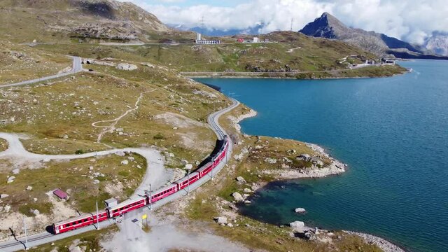 Aerial drone footage of a train travelling along the lake at the summit of the Bernina pass in the alps in Canton Graubunden in Switzerland. Shot with a following motion. 