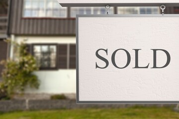 Estate agent SOLD sign with the defocussed street of houses in the background