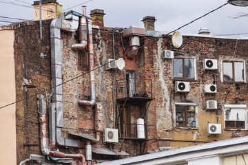 Back wall of a brick building with hanging air conditioners. The courtyard of an old house with pipes, wires, ventilation and antennas.