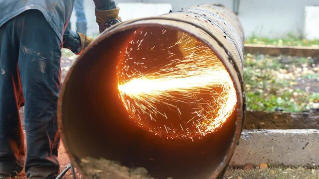 The welder cuts a large diameter metal pipe and sparks fly. Work as a welder on the street.