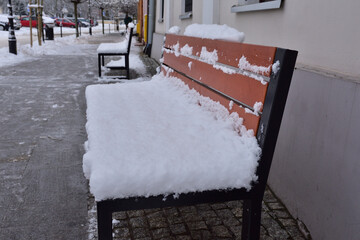 A bench covered with snow against the wall of a building in a city on a gloomy winter day. Winter.