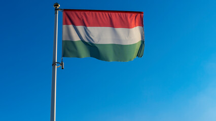 National flag of Hungarian on a flagpole in front of blue sky with sun rays and lens flare. Diplomacy concept.