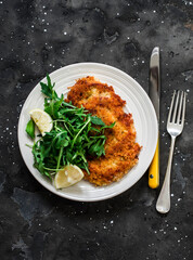 Garlicky bread crumbs crispy turkey schnitzel and fresh lemon arugula salad on a dark background, top view