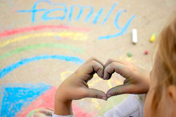 selective focus on the hands of the child showing the heart on the background of the chalk lettering family and the drawn rainbow, love and care within the family