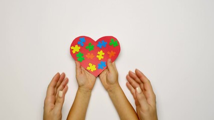 Maternal love, care and affection for children, regardless of their social status. A heart with puzzles inside in the hands of a baby and the support of a mother. World awareness Autism day