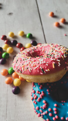 Close up of assorted glazed doughnuts with sprinkles and candies, frosted donuts on wooden background, sweet donuts with sugar icing and sprinkles, unhealthy food, blue and pink glazed doughnuts