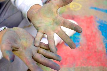 selective focus on the hands of a child soiled with chalk after drawing pictures on the asphalt against the background of a painted red house, creativity of children on the street