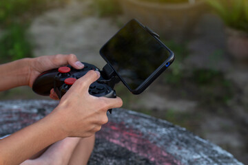 Hand of child holding a joystick connect to mobile phone playing console game in the garden.