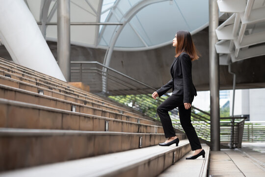 An Asian woman in a suit is walking up stairs outdoors.