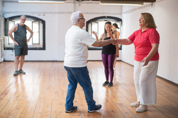 Fototapeta na wymiar Senior Caucasian couple learning dance steps in studio. Retired partners wearing glasses dancing in class with teacher doing rhythm clapping. Dance, hobby, healthy lifestyle concept