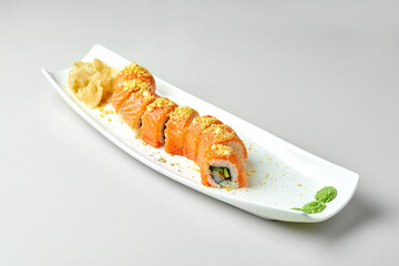 Sushi roll golden dragon with salmon and avocado in a white plate on a gray background