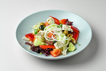 Vegetable salad with tomatoes, feta and olives in a gray plate on a gray background. Greek salad