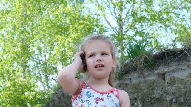 Little girl holding smartphone near her ear and listening to music . Child dancing to music outdoors