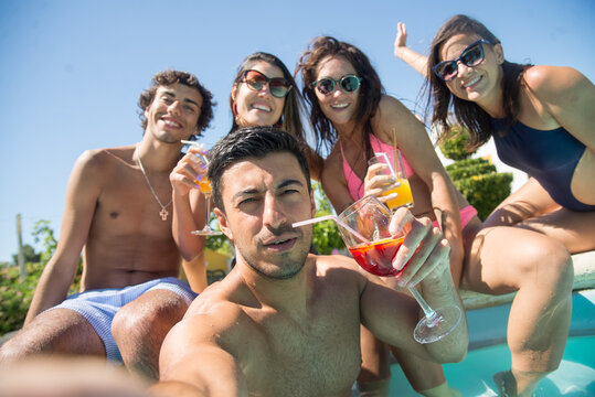 Relaxed friends taking selfie at poolside. Women and men in swimsuits resting in swimming pool, taking pictures with camera. Leisure, friendship, party concept