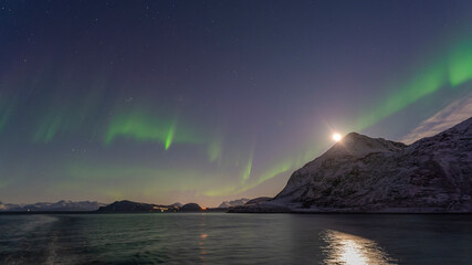 Fototapeta na wymiar tanzende Nordlichter über den Lyngenalps in Norwegen, mit Vollmond. Aurora Borealis an einem hellen Herbstabend über verschneiten Bergen auf der Kreuzfahrt nach Tromsø.