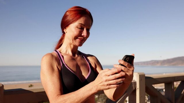 62 year old woman taking a break from her workout to check her social media. At the beach in Santa Monica California.