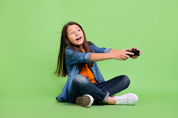 Full length photo of impressed small girl play station look promo wear shirt jeans shoes isolated on green background