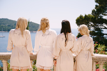 Bride and her bridesmaids stand on the balcony and look at the sea