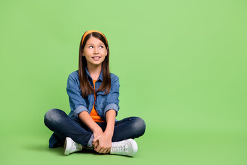 Full size photo of nice little girl sit look promo wear shirt jeans hairband footwear isolated on green background